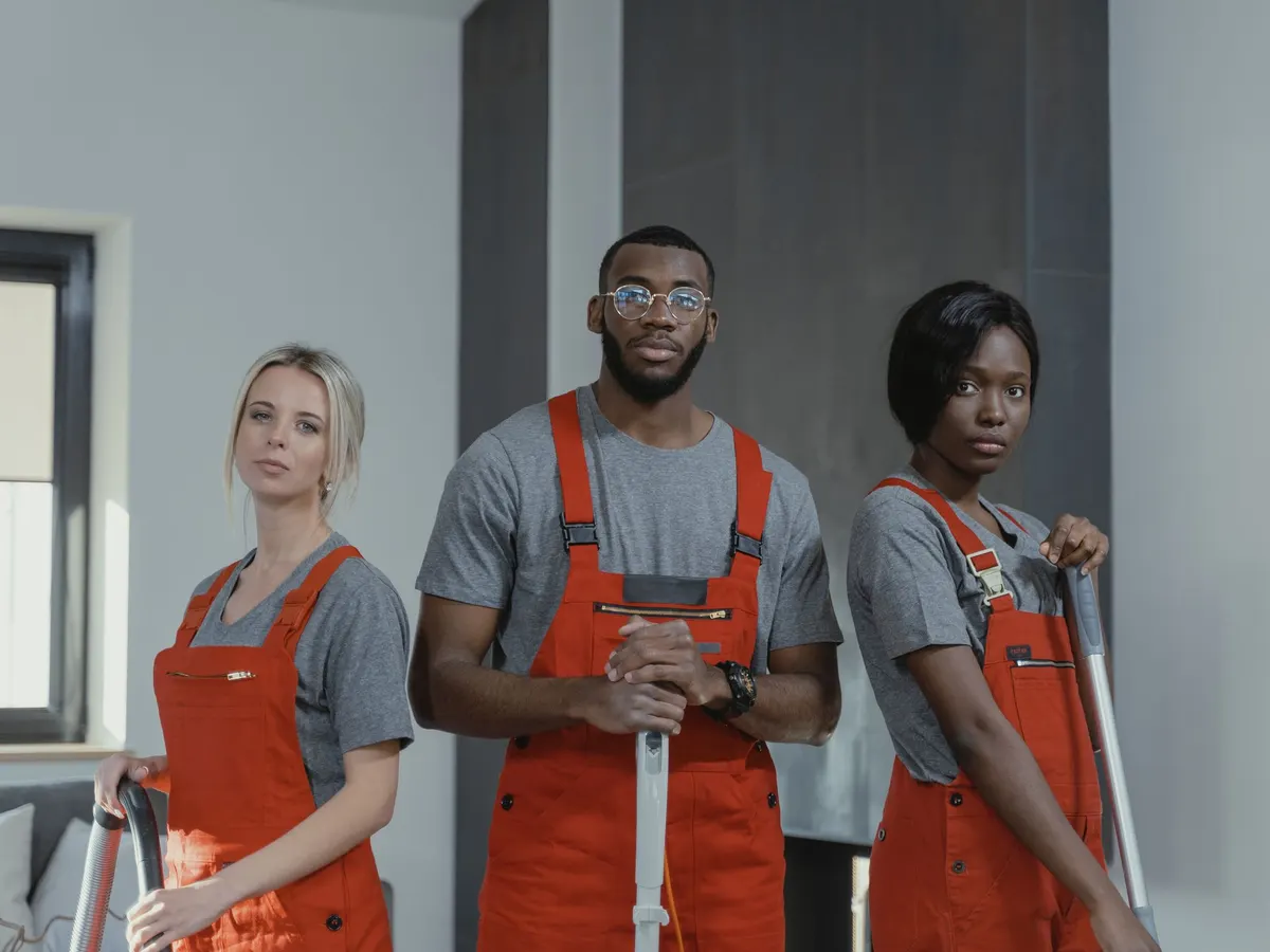 Three cleaning professionals in uniform holding cleaning equipment